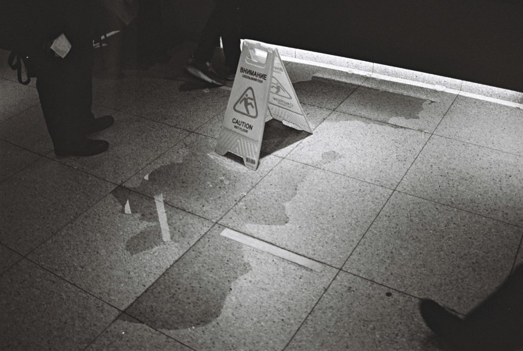 Black and white image of caution sign on wet floor in indoor setting.