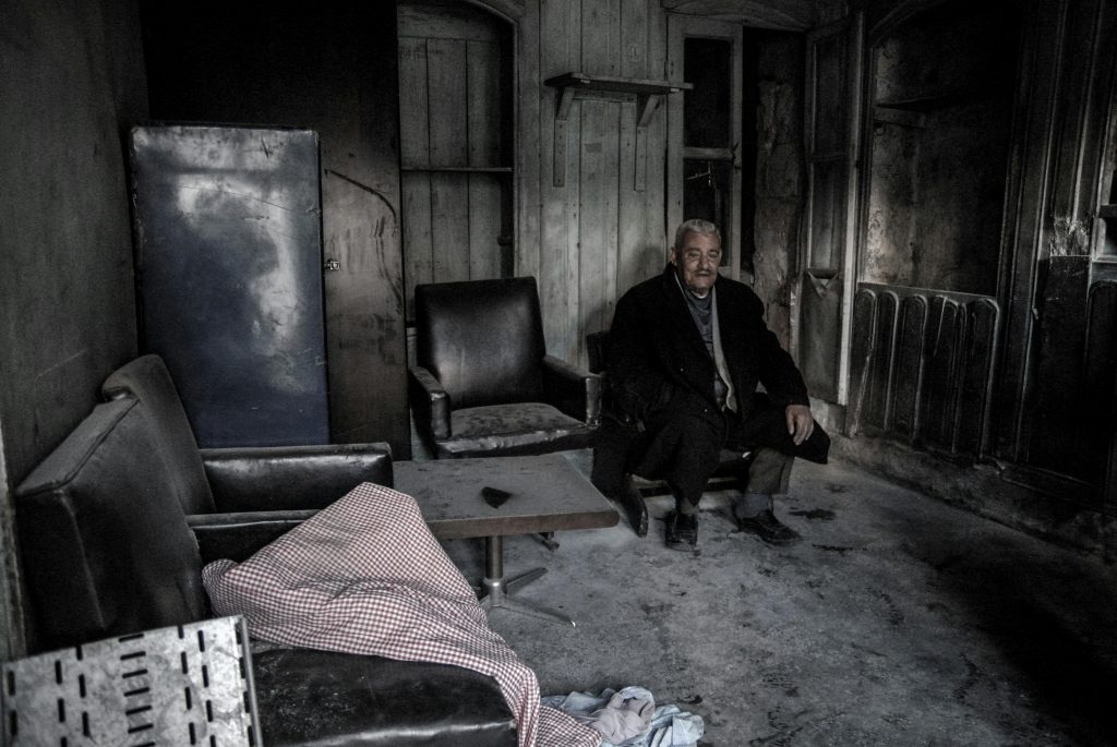 Portrait of a man sitting thoughtfully in a burnt, deserted living room.