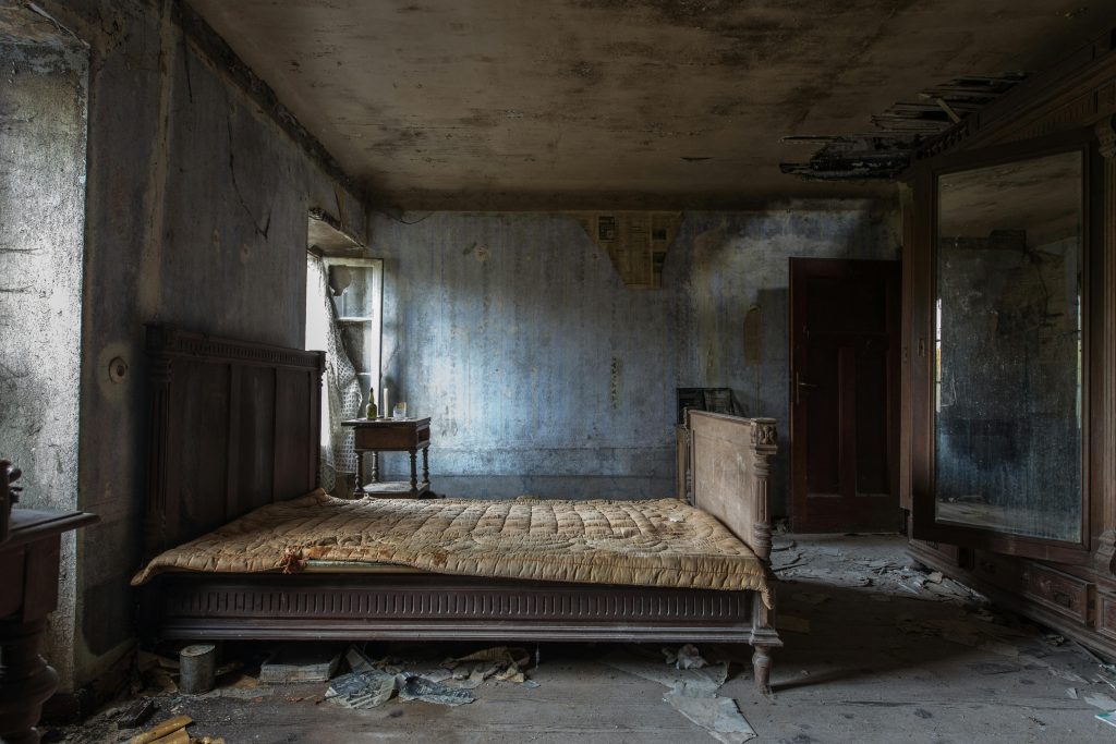 Explore the haunting beauty of an abandoned rustic bedroom, displaying decayed furniture and peeling walls.