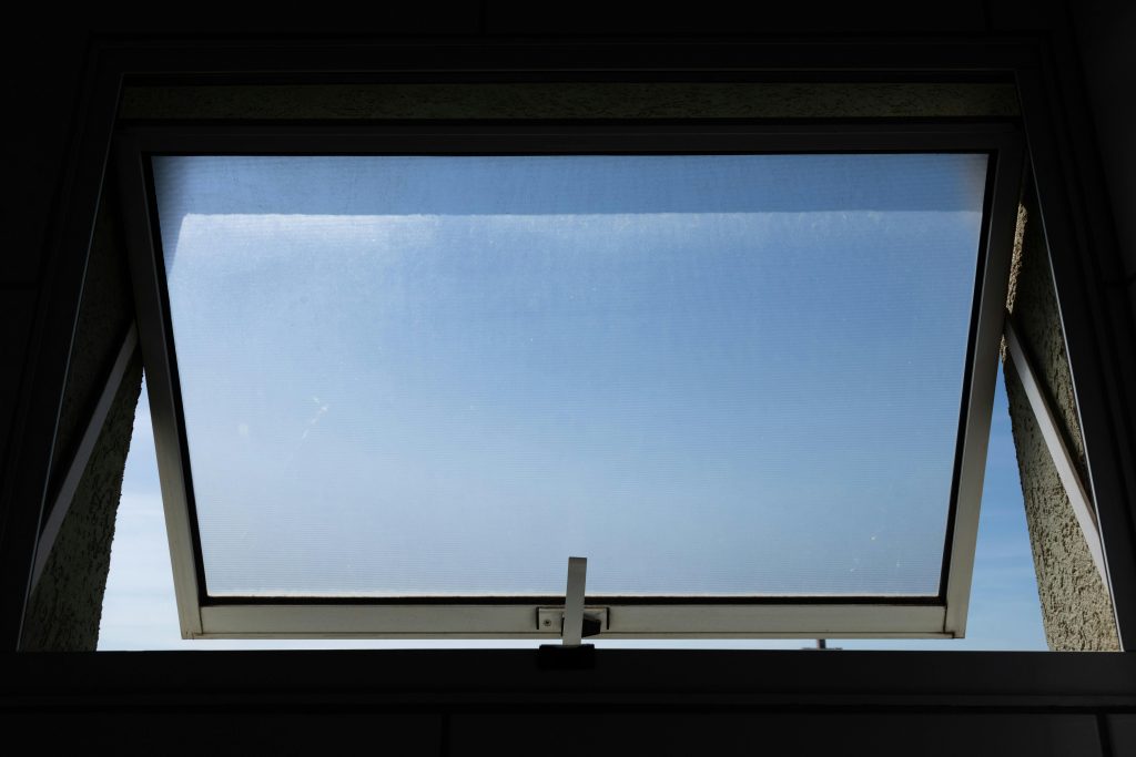 A low angle view of an open skylight window revealing a clear blue sky.