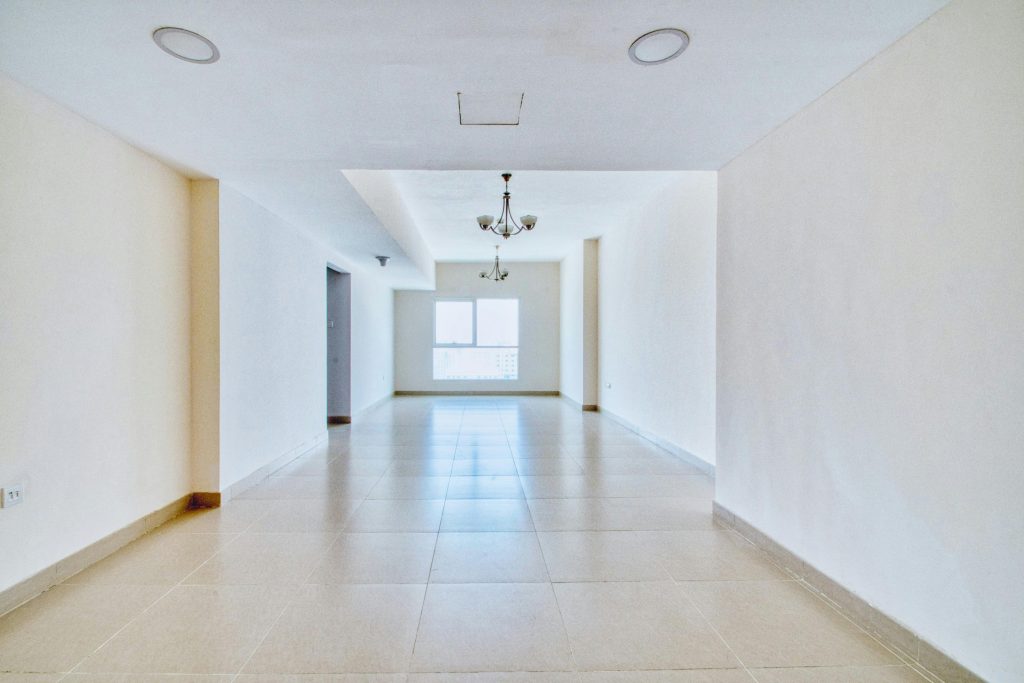 Bright, empty apartment interior featuring large windows, tiled floor, and a chandelier.